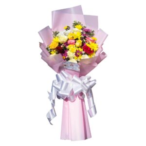 A colorful flower bouquet with yellow, white, pink, and red blooms, wrapped in a soft pink wrapper and tied with a large white ribbon