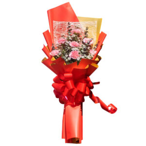 Handcrafted pink carnation flower bouquet with white filler flowers, wrapped in vibrant red and gold wrapping.